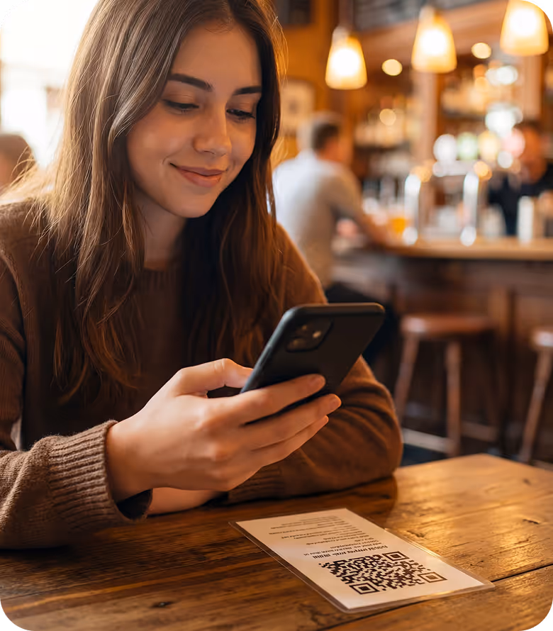 Junge Frau in braunem Pullover liest QR-Code auf einem Tisch in einem gemütlichen Café.
