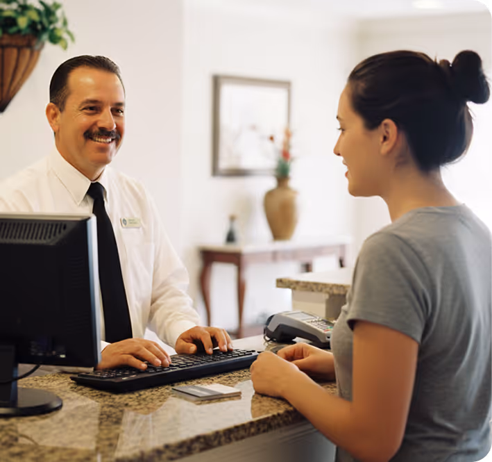 Ein freundlicher Hotelmitarbeiter an der Rezeption spricht mit einer weiblichen Gästin.