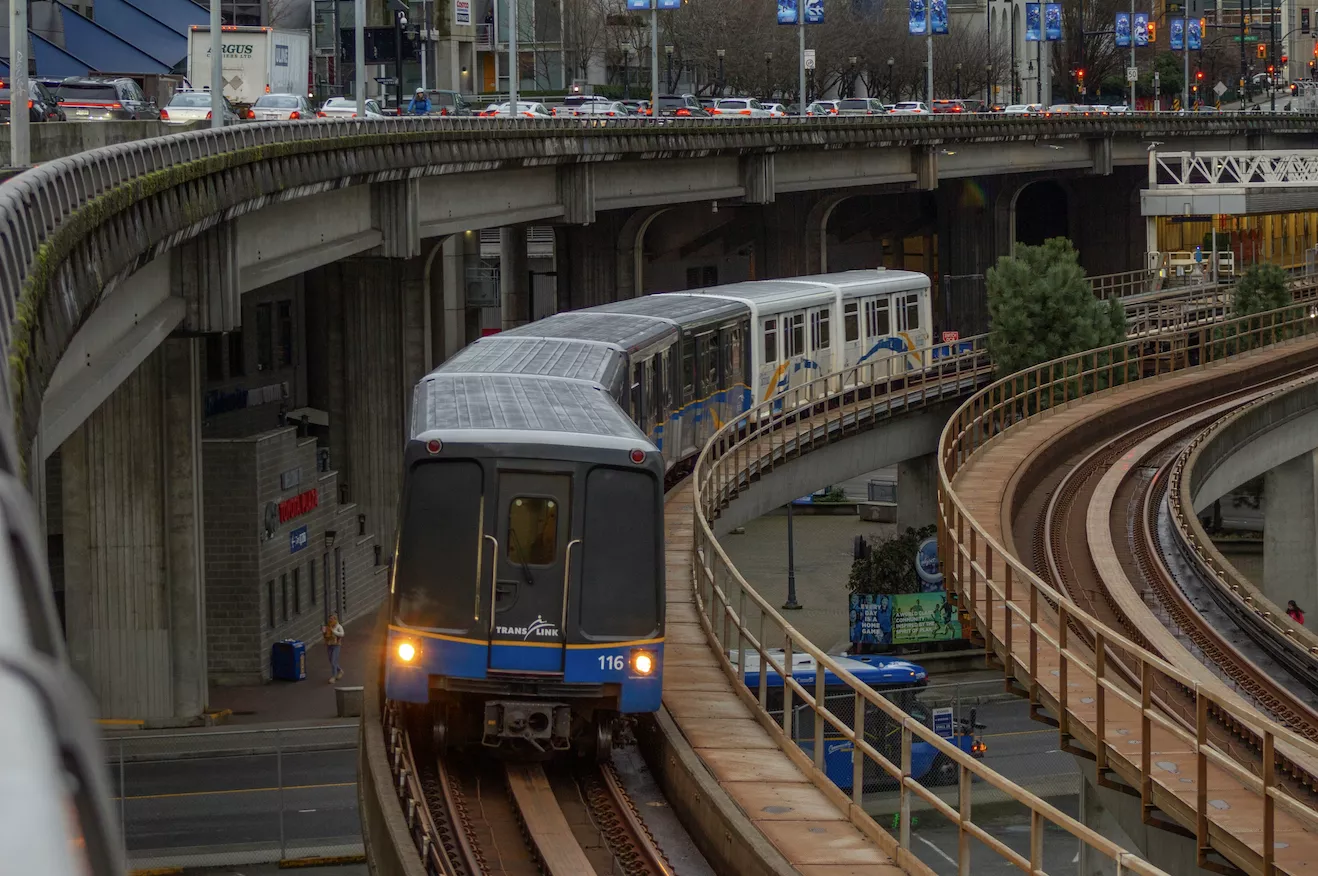 Skytrain traveling down train tracks next to a bridge