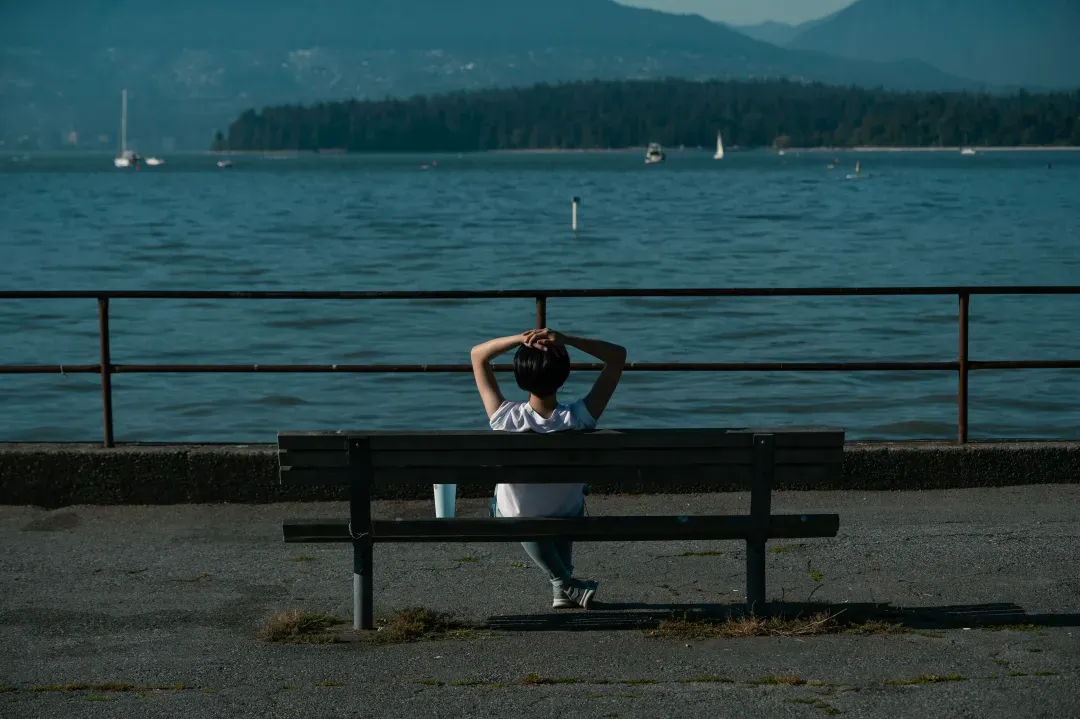 Woman sitting on a bench by the Vancouver coast enjoying the serene ocean view.