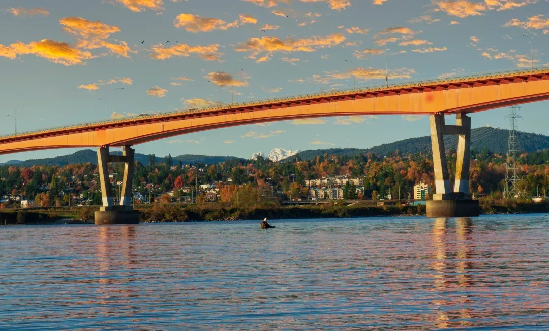 A scenic sunset view of a bridge over the Fraser River in Vancouver, BC, Canada.