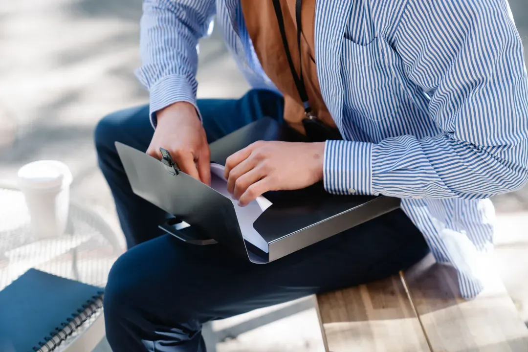 Professional reviewing documents in a folder while sitting outside, dressed in business attire.