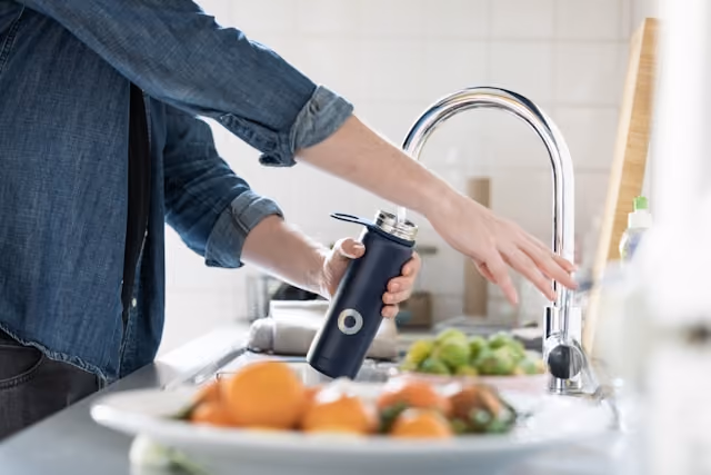 Traveller filling a reusable water bottle from a kitchen tap in a destination with safe drinking water