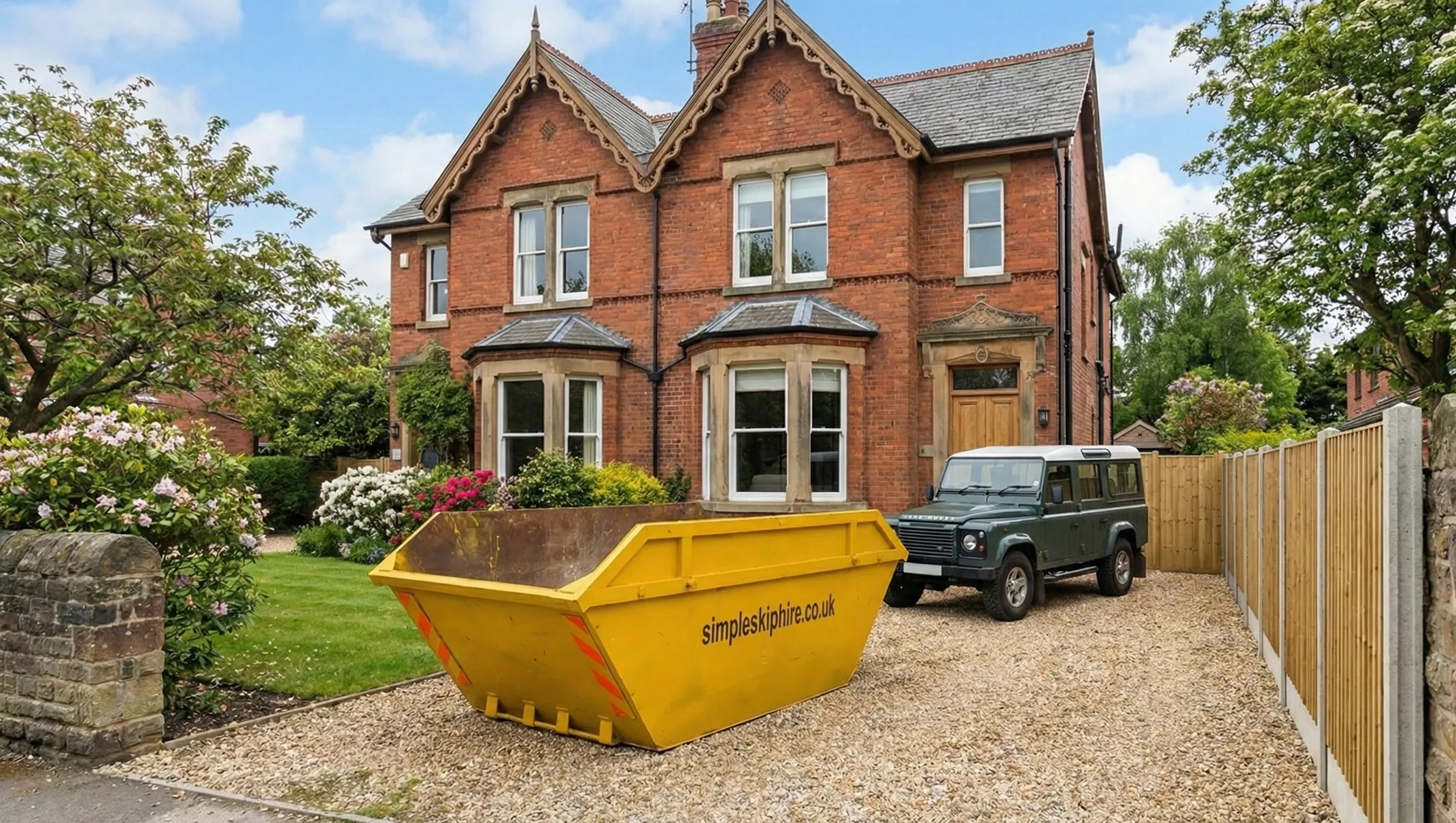 Yellow skip with simpleskiphire.co.uk logo on gravel driveway of a brick house with bay windows and a dark green Land Rover parked beside it.