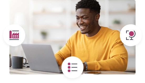 Smiling man in a yellow sweater using a laptop at a desk with a coffee mug nearby.