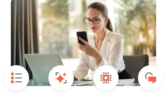 Jovem mulher de óculos e camisa branca sentada à mesa usando smartphone com laptop ao fundo.