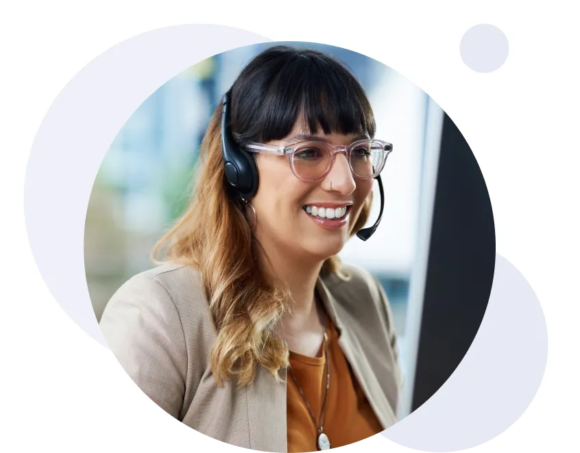 Femme souriante portant des lunettes et un casque audio, travaillant sur un ordinateur dans un bureau.