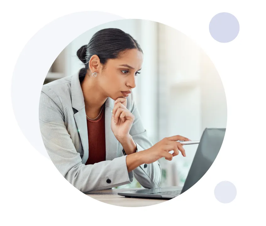 Une femme en blazer pointe attentivement un stylo vers l'écran d'un ordinateur portable tout en réfléchissant.