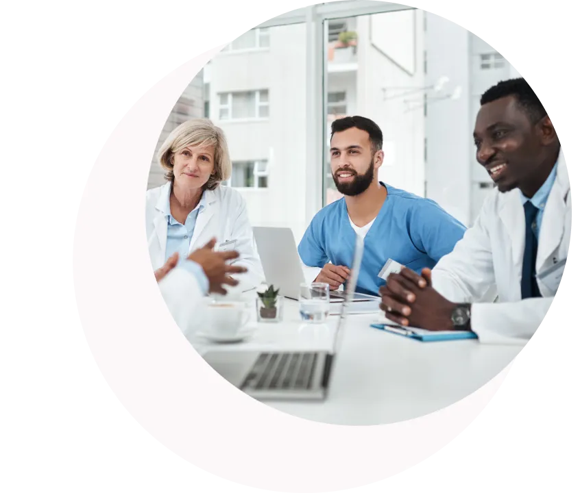 Tres profesionales sanitarios, entre ellos dos médicos y una enfermera, sentados a una mesa discutiendo con ordenadores portátiles y documentos.