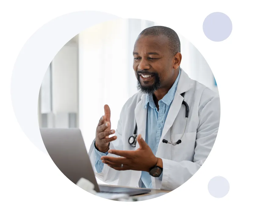 Médico sonriente con bata blanca y estetoscopio consultando a través de un ordenador portátil en una videollamada.