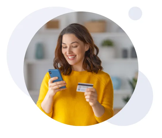 Smiling woman in yellow sweater holding a credit card and looking at her smartphone.