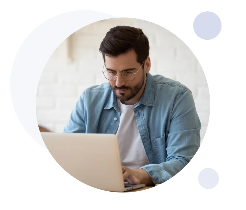 Hombre con gafas y chaqueta vaquera concentrado en trabajar con un ordenador portátil en interiores.