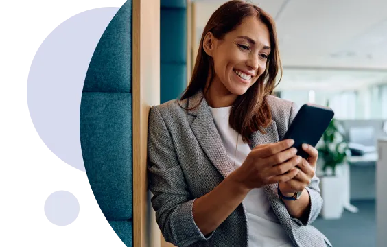 Mujer de negocios sonriente con una chaqueta gris mirando su smartphone en una oficina moderna.