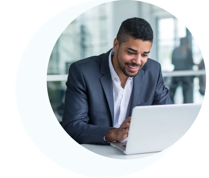 Hombre sonriente con traje oscuro trabajando con un ordenador portátil en una oficina moderna.