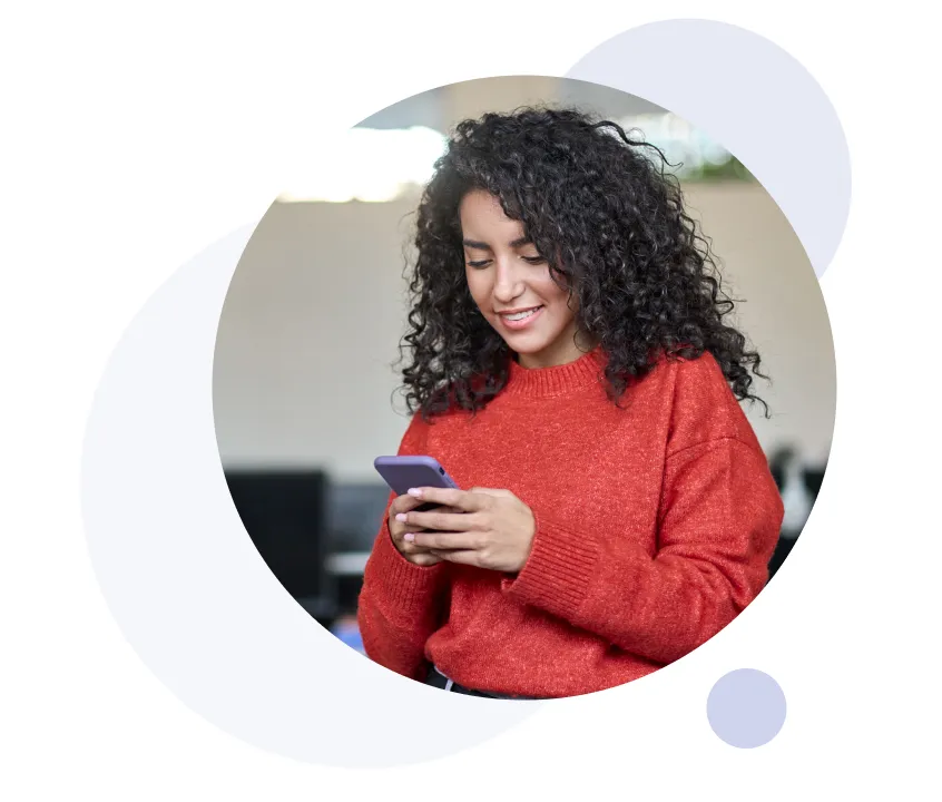 Mujer sonriente con cabello rizado, vistiendo un suéter rojo, usando un teléfono inteligente.