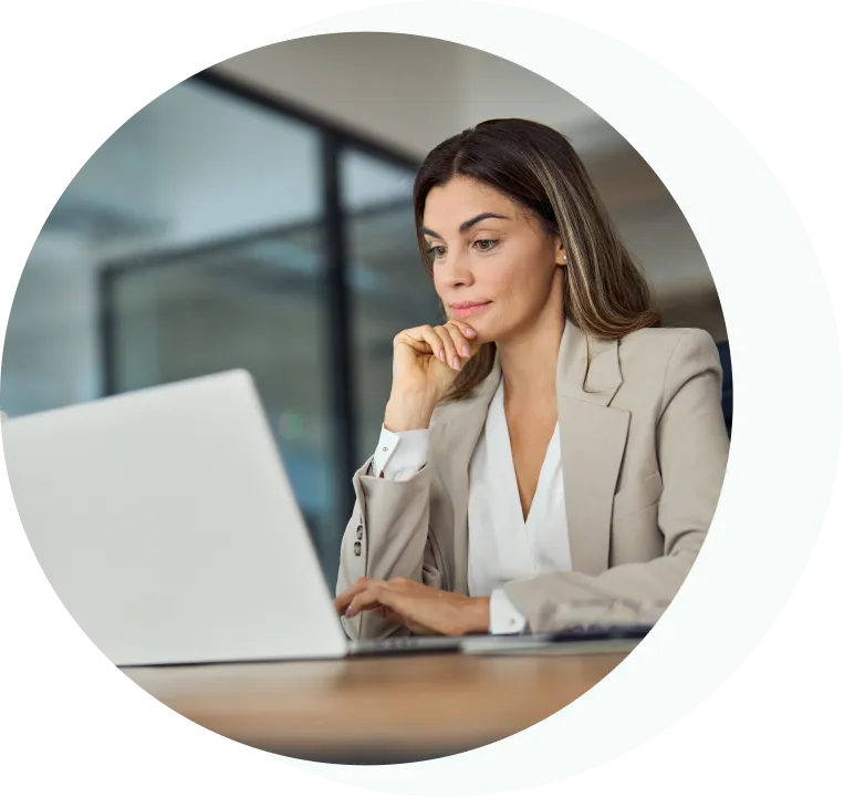 Professional woman in a beige blazer working on a laptop in a modern office.