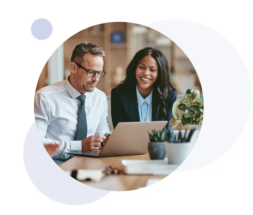 Two business professionals, a man and a woman, looking at a laptop together in an office setting.