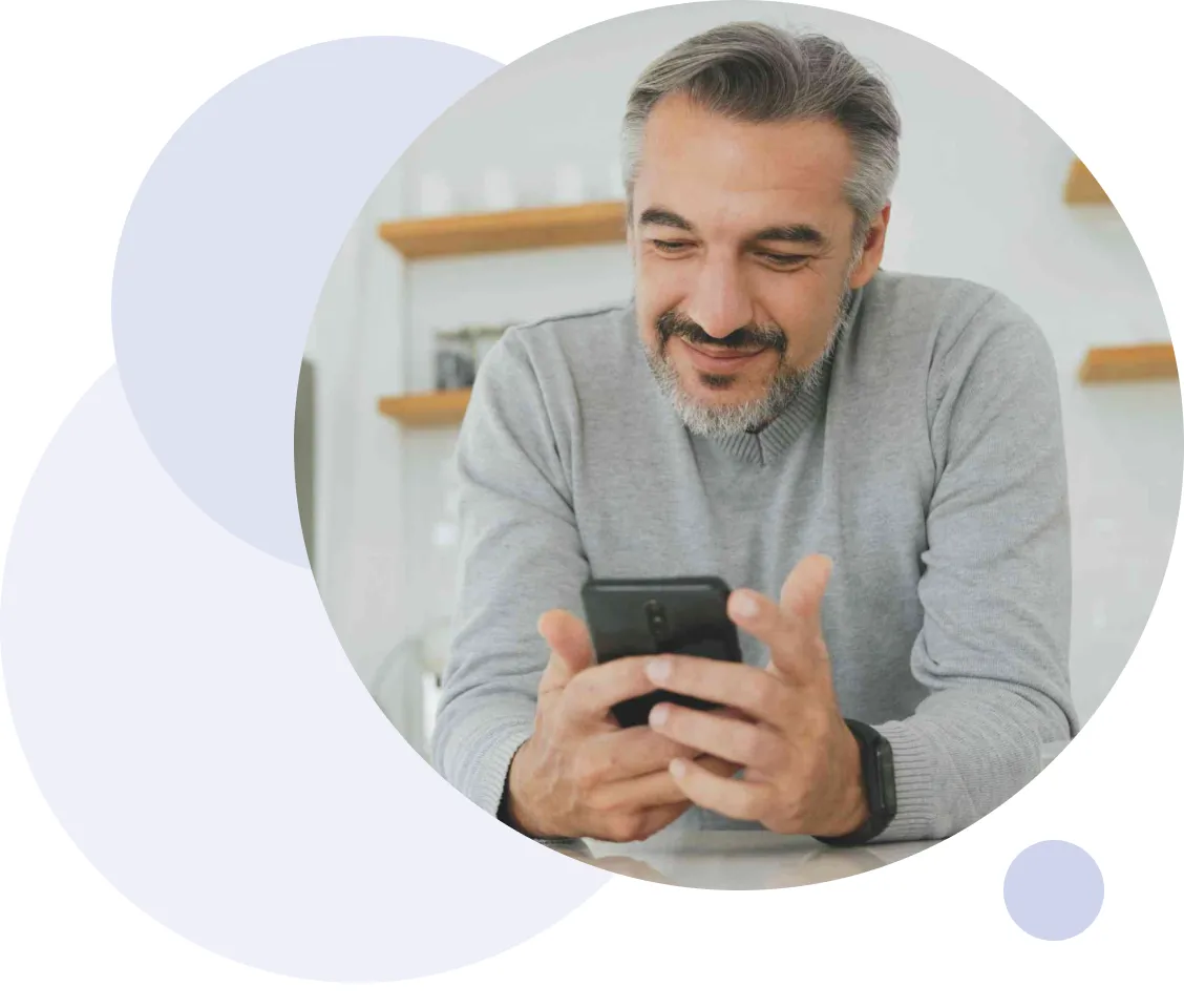 Homme en pull gris souriant tout en regardant son smartphone à l'intérieur.