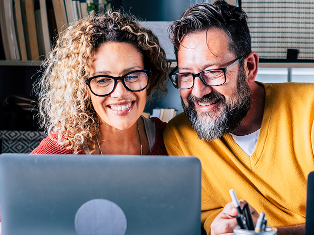 Two smiling colleagues looking at a laptop screen together in an office
