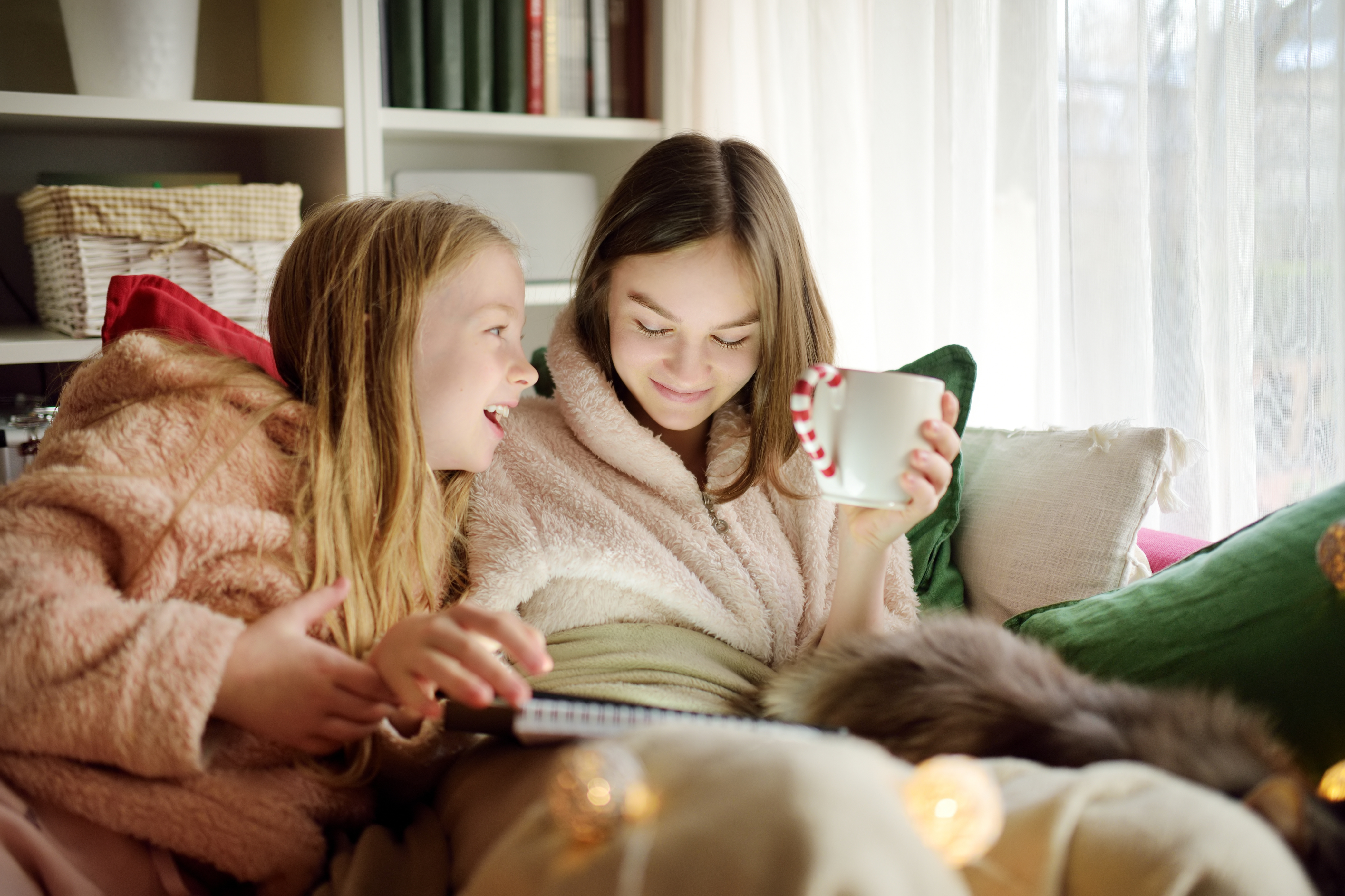 Two young sisters snuggling up on the sofa in a cozy living room.