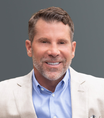 Smiling middle-aged man with short brown hair, beard, wearing a light beige blazer and blue shirt.