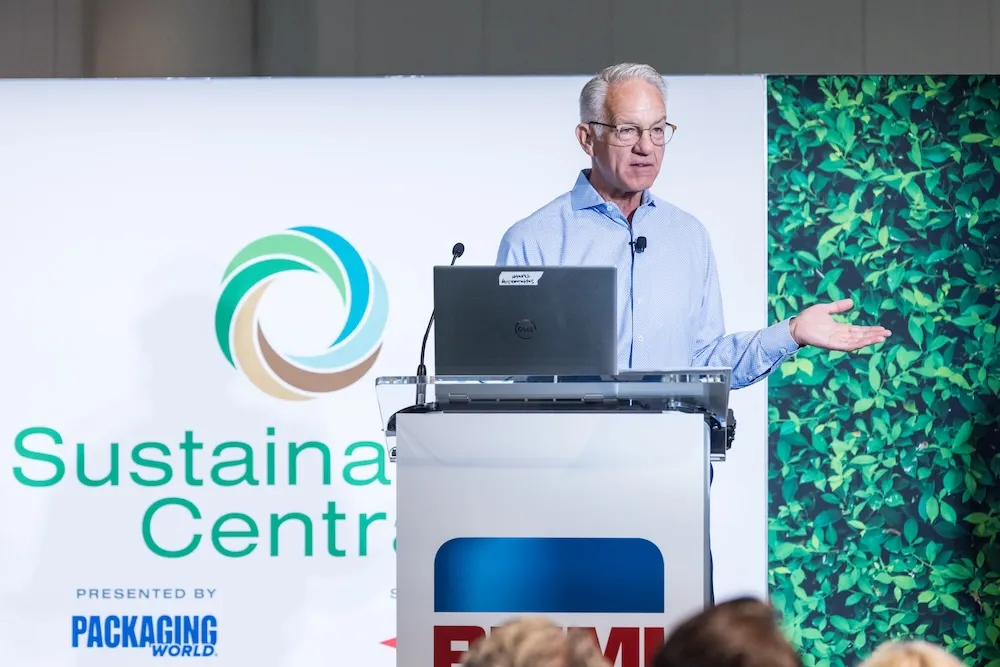 Man speaking at a podium with a laptop, in front of a screen showing the Sustainable Central logo and packaging world branding.