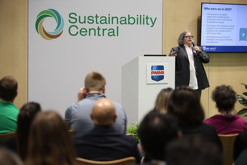Woman speaking at a Sustainability Central event with a presentation slide behind her and audience seated in front.