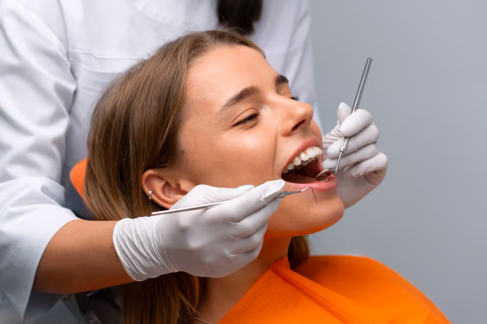 Dentist wearing white gloves examining a smiling patient's teeth using dental tools.
