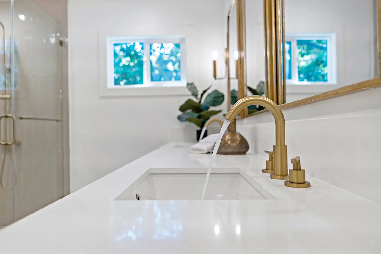 High-end bathroom vanity area by Enhaus Design & Build, featuring a large arched brass mirror against a white fluted accent wall, illuminated by warm sunset light.
