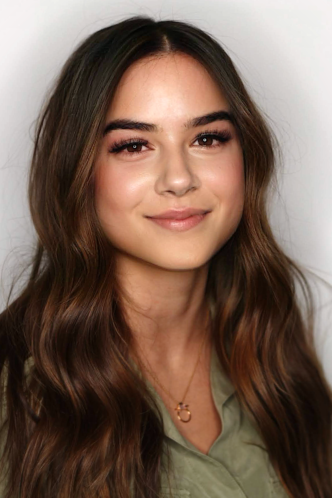 Smiling young web developer with long wavy brown hair wearing a green shirt and a circular pendant necklace.