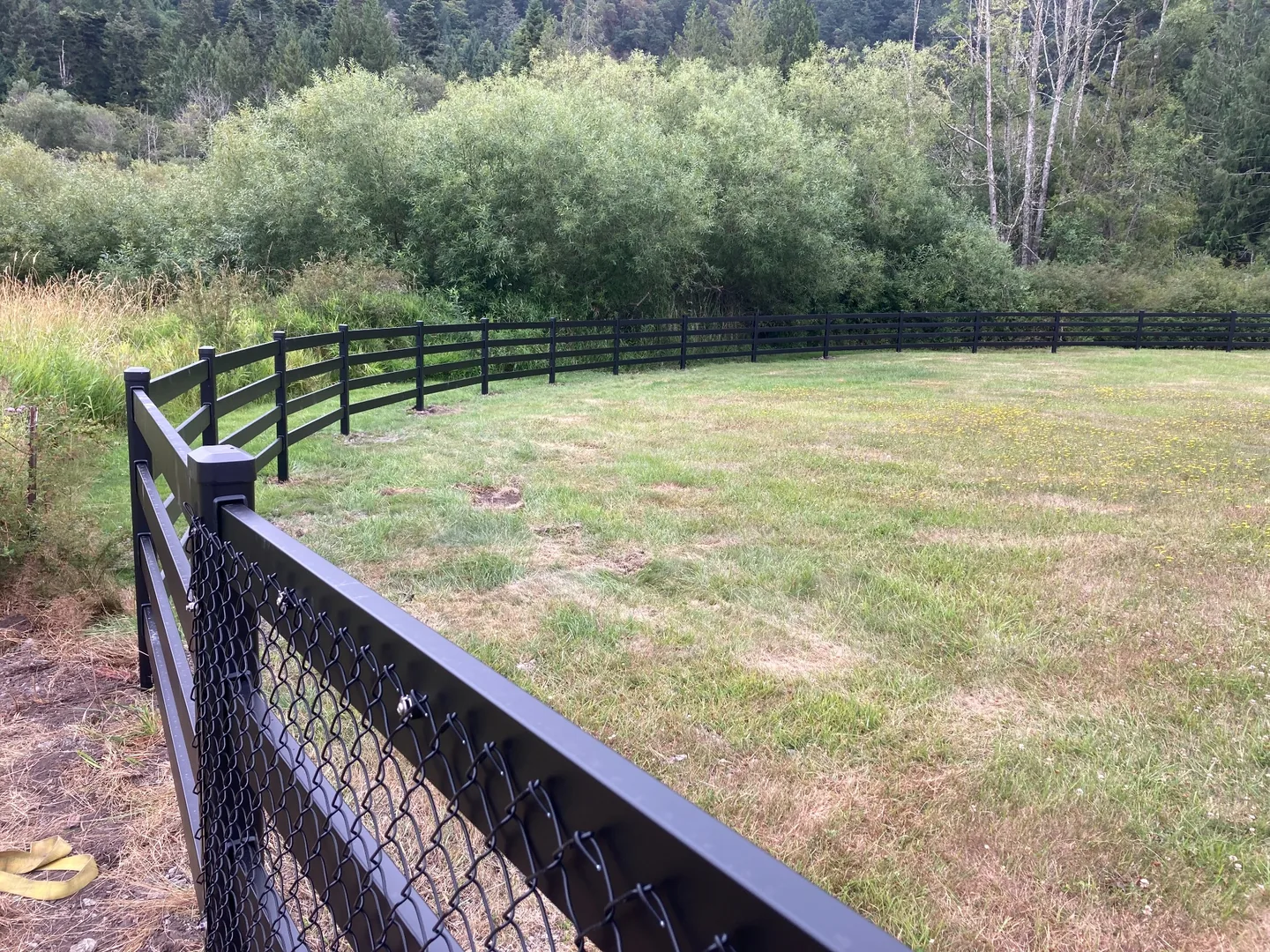 Curving black Buckley Steel Board fence following the field edge on San Juan Island