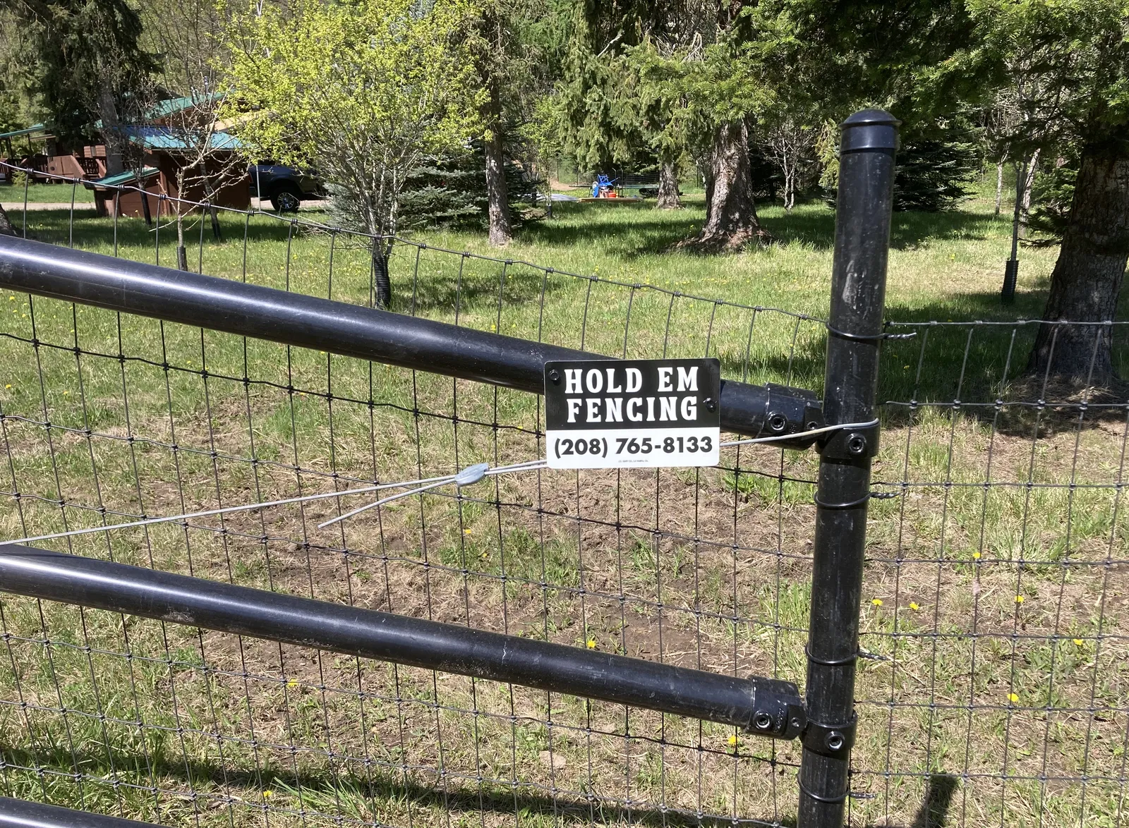 Close view of black no-climb mesh, black steel pipe, and a Hold Em Fencing project sign.