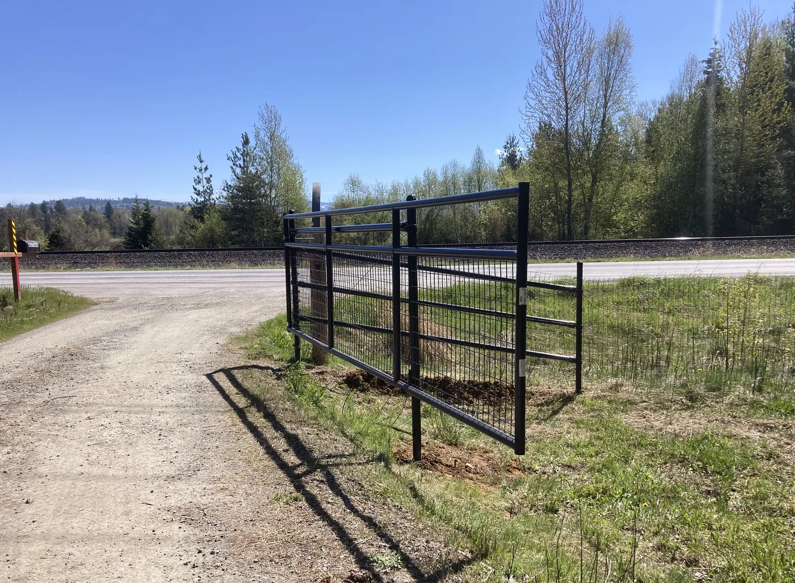 Black Frontier mesh gate beside the gravel driveway at the North Idaho property.
