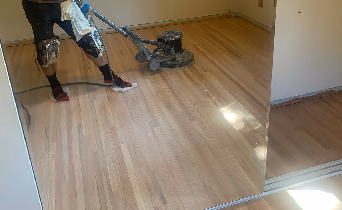 Hardwood floors in the process of being buffed with worker operating machine