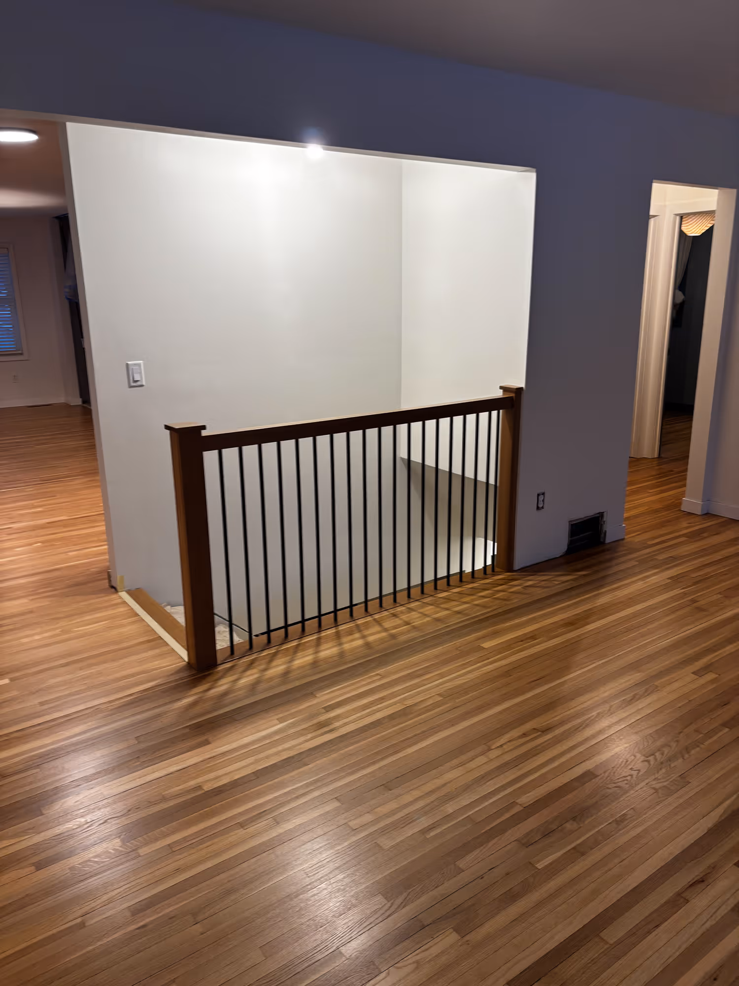 Newly refinished hardwood floors in a living room with a metal banister on the stairway leading downstairs