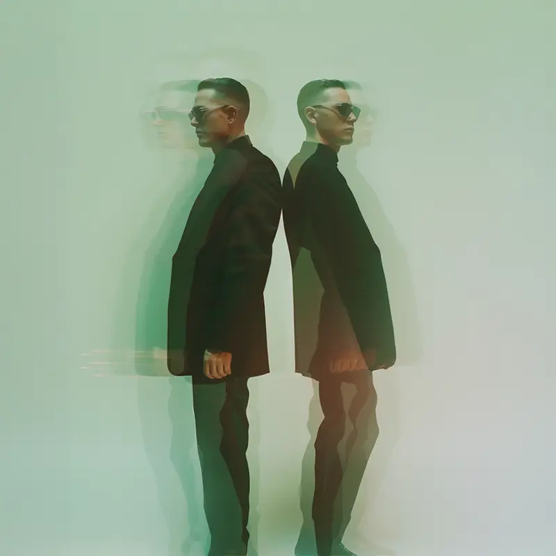 Two figures in motion blur standing against a muted green background.