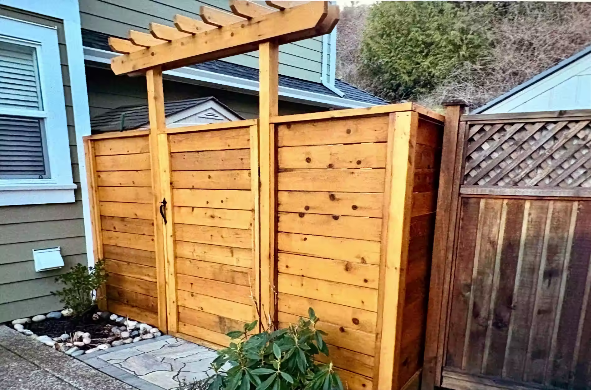 Cedar privacy gate with pergola top beside house, with stone path and small shrubs