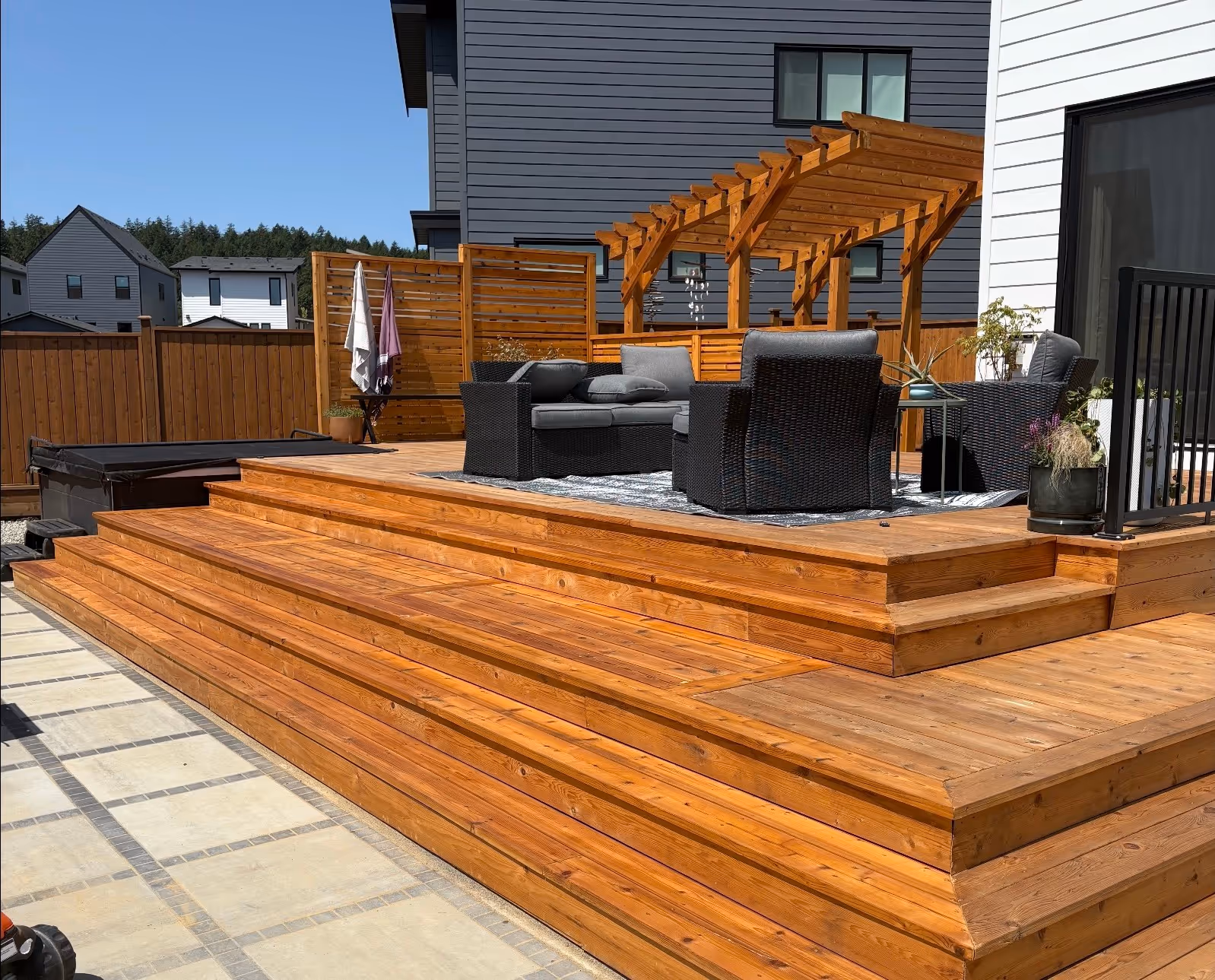 Wood backyard deck with wide steps, pergola, privacy screen, outdoor seating, and hot tub