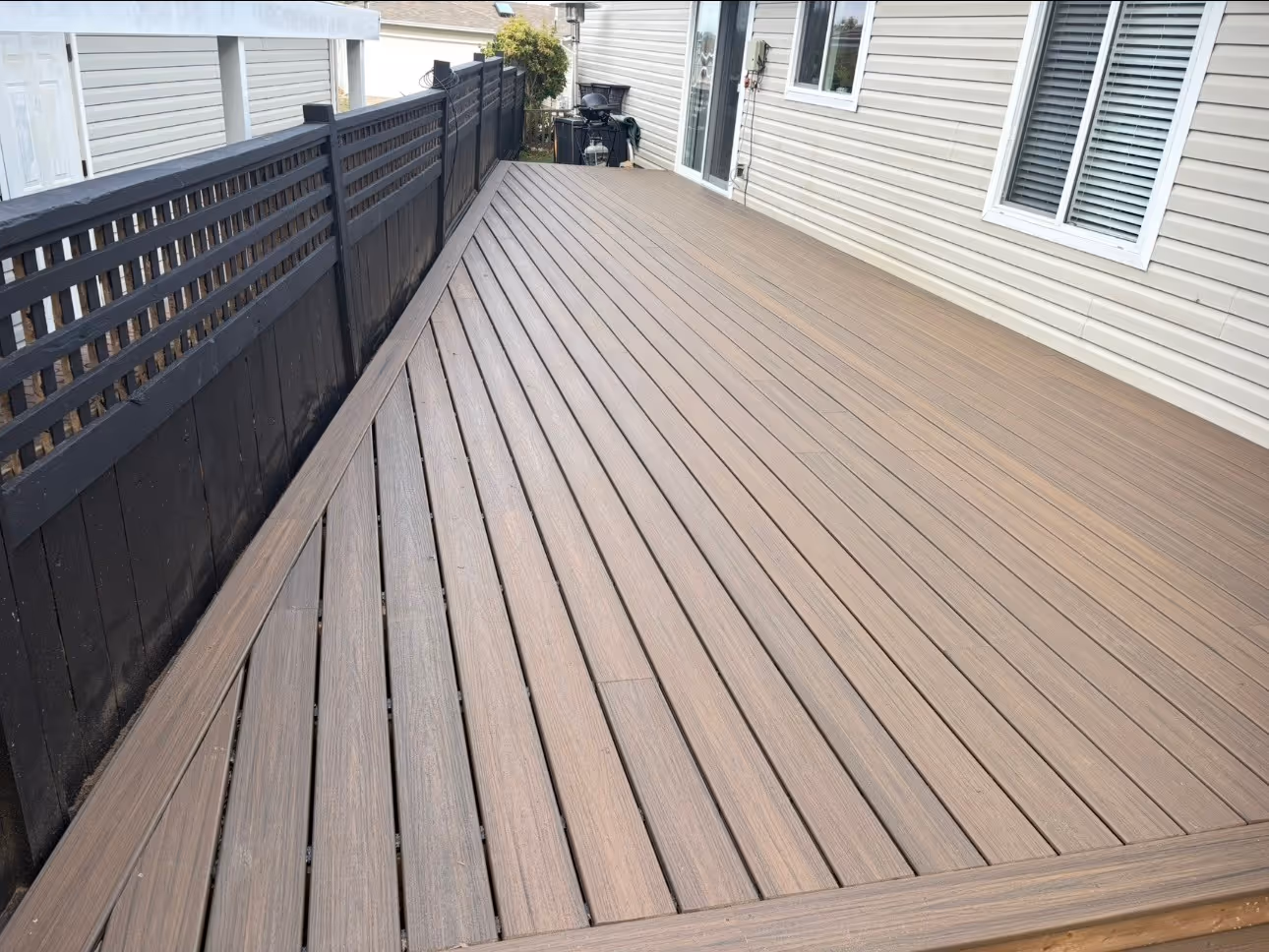 Brown composite deck alongside a house with black fence and diagonal board pattern