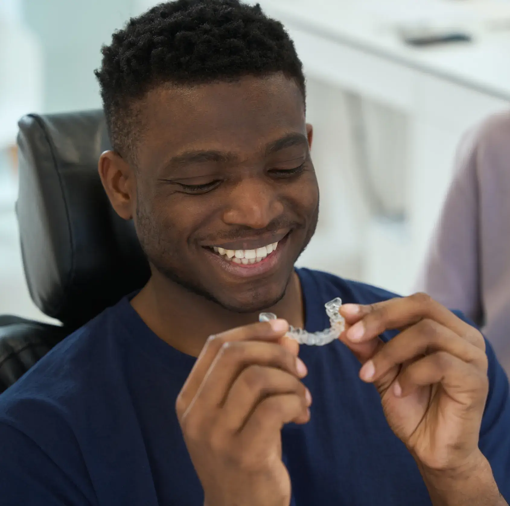 Smiling man holding a clear dental aligner in a dental office.