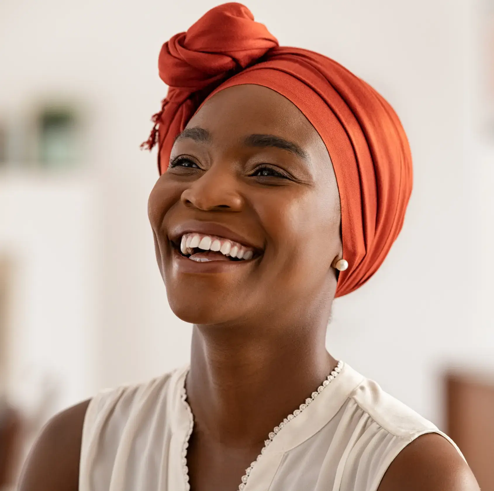 Smiling woman wearing an orange headwrap and pearl earrings.