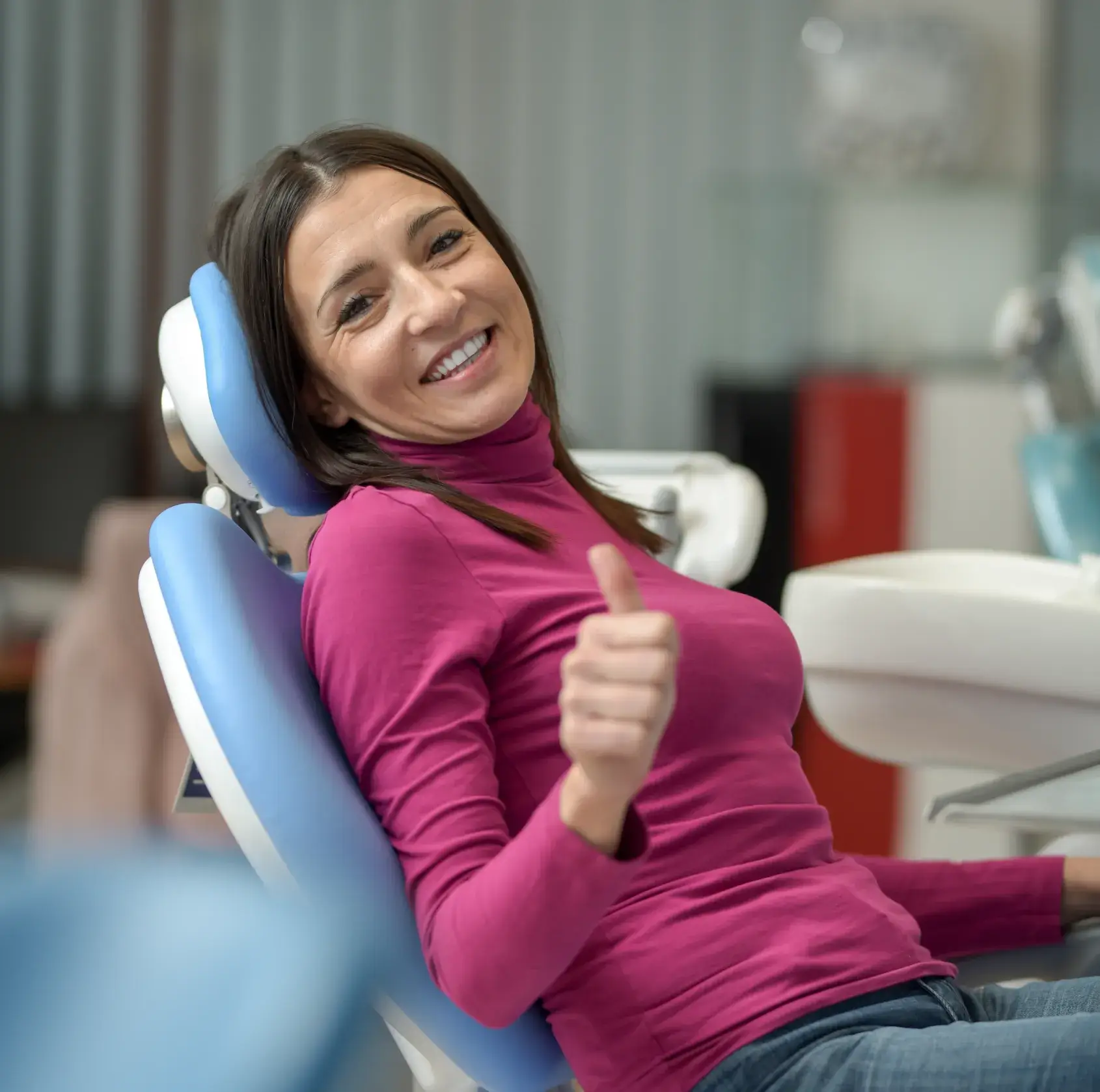 Smiling woman in a magenta top giving a thumbs-up while sitting in a dental chair.