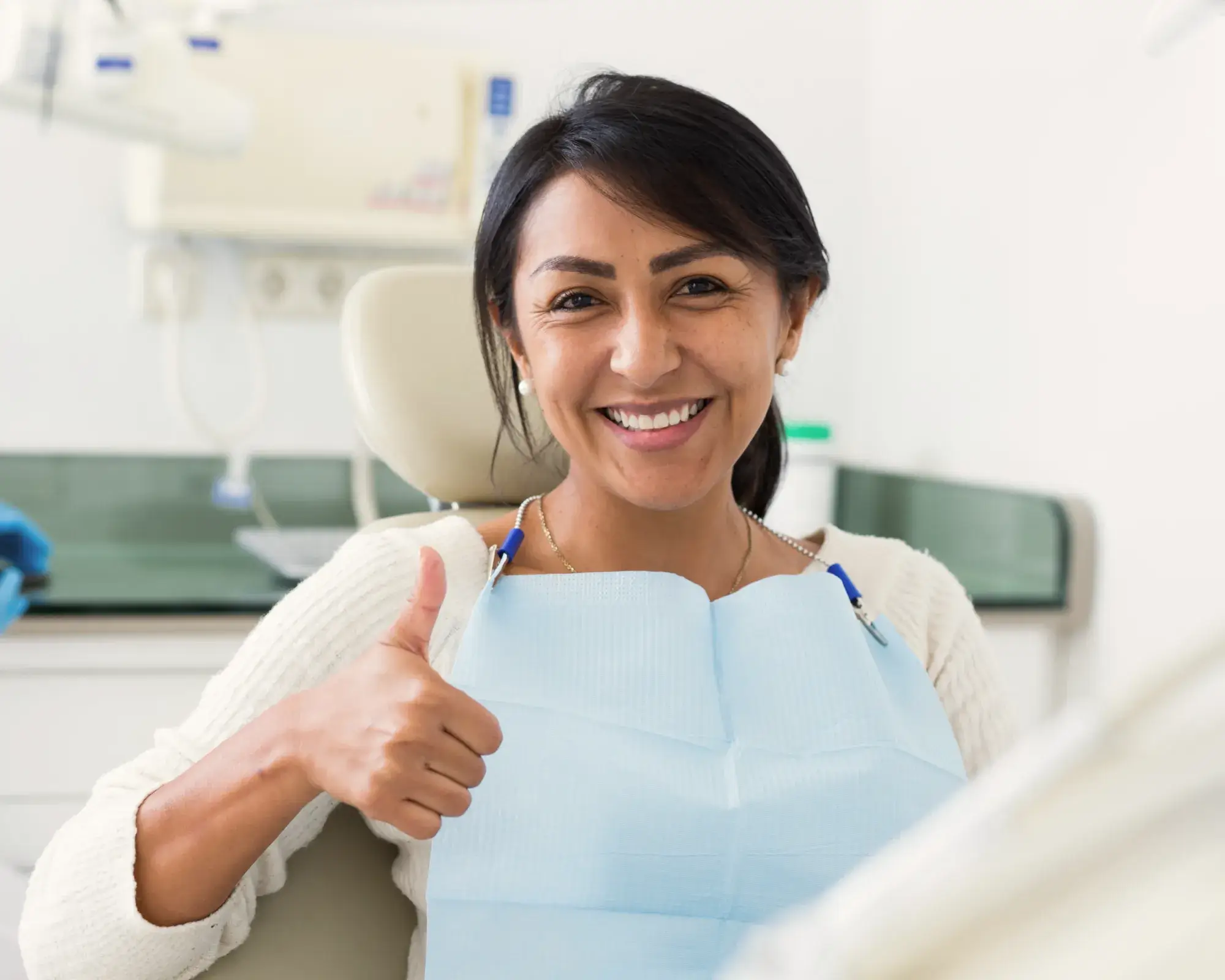 Smiling woman in a dental chair giving a thumbs up wearing a dental bib.