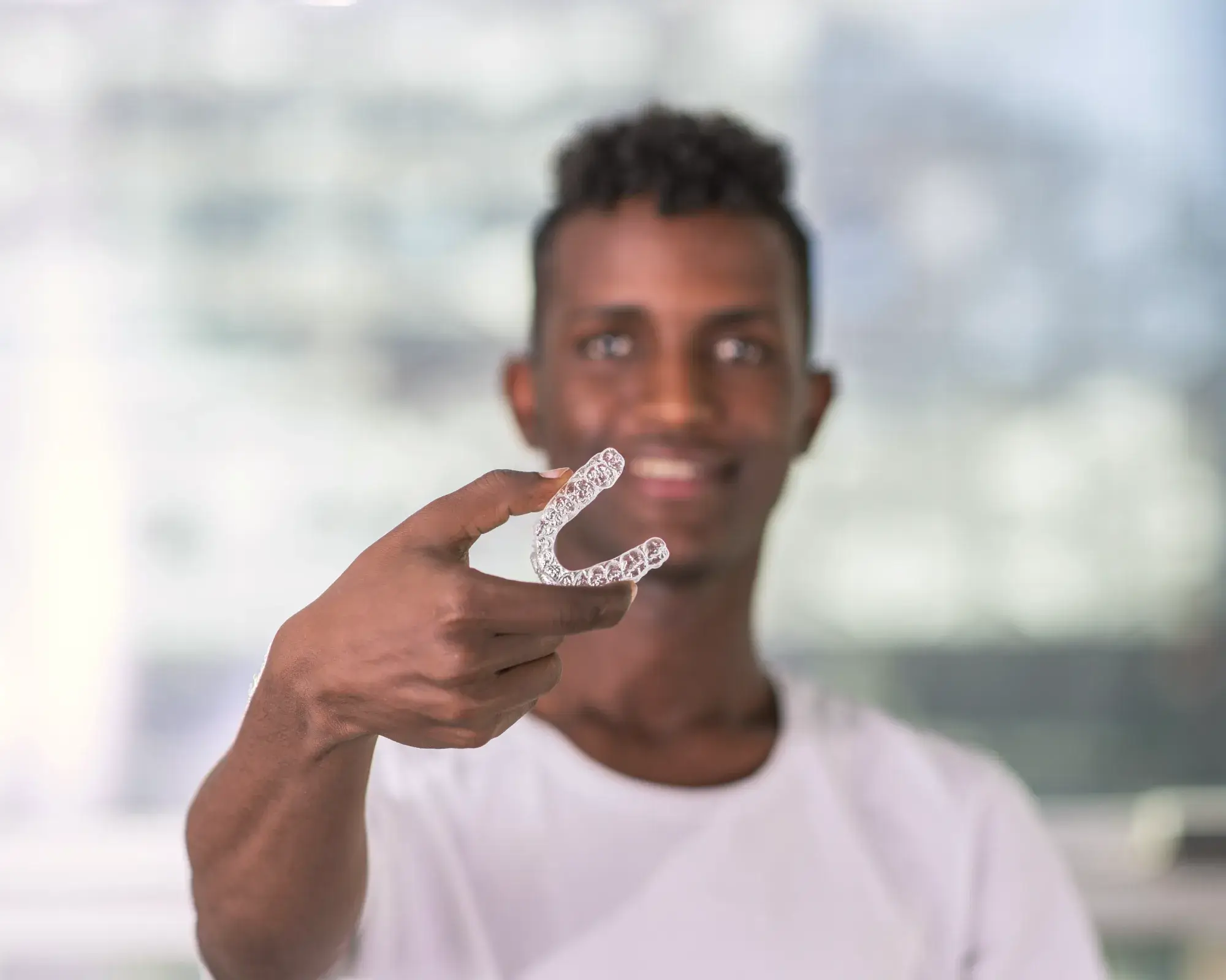 Man holding a clear dental aligner in front of him, smiling.