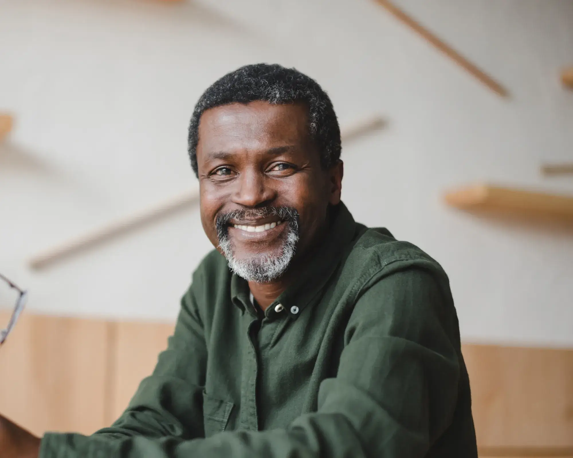 Smiling middle-aged man with salt-and-pepper beard wearing a green button-up shirt indoors.