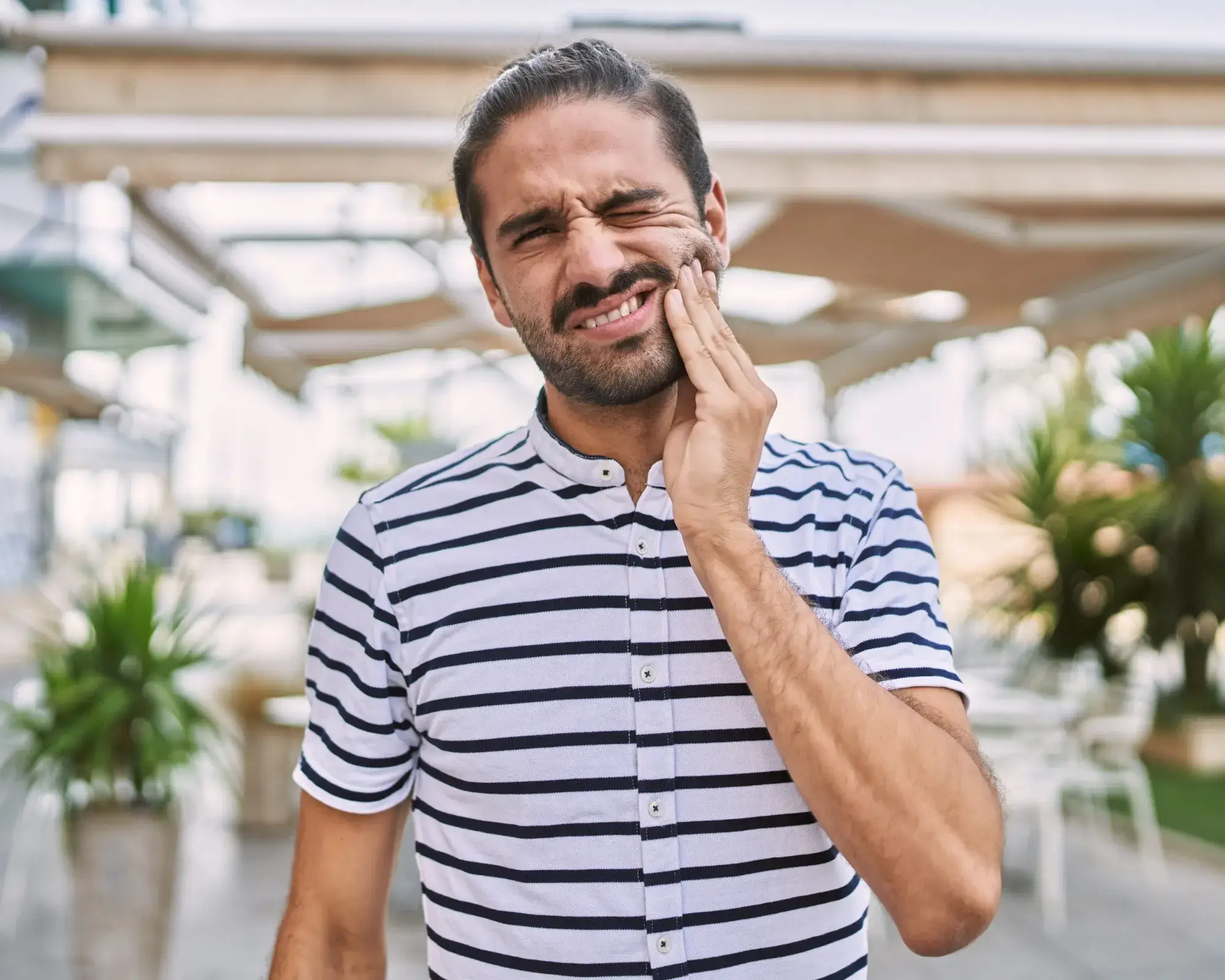 Man in a striped shirt holding his cheek in pain, indicating a toothache or jaw discomfort.