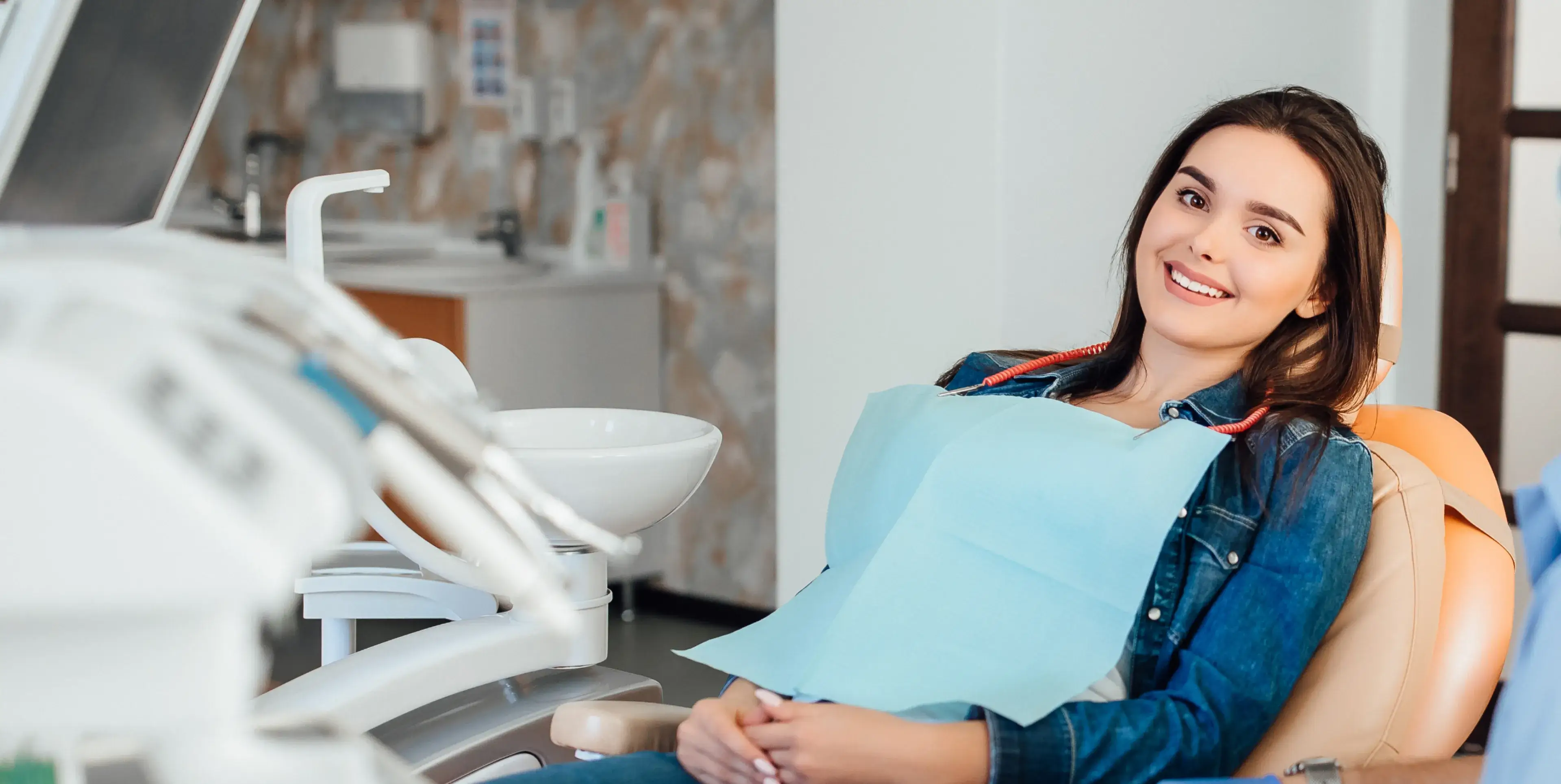 Smiling young woman wearing a dental bib reclining in a dental chair in a clinic.
