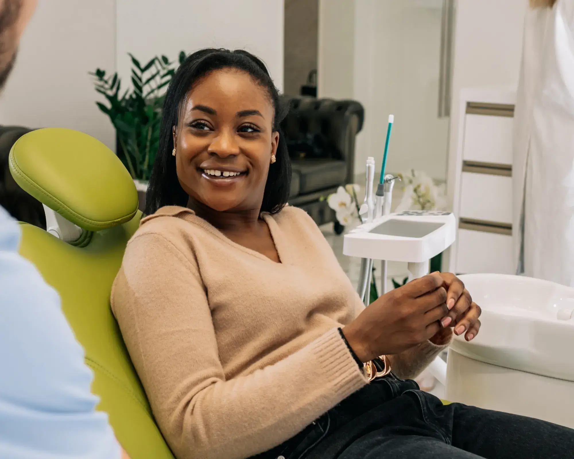 Smiling woman sitting in a green dental chair, talking to a person in a dental office.