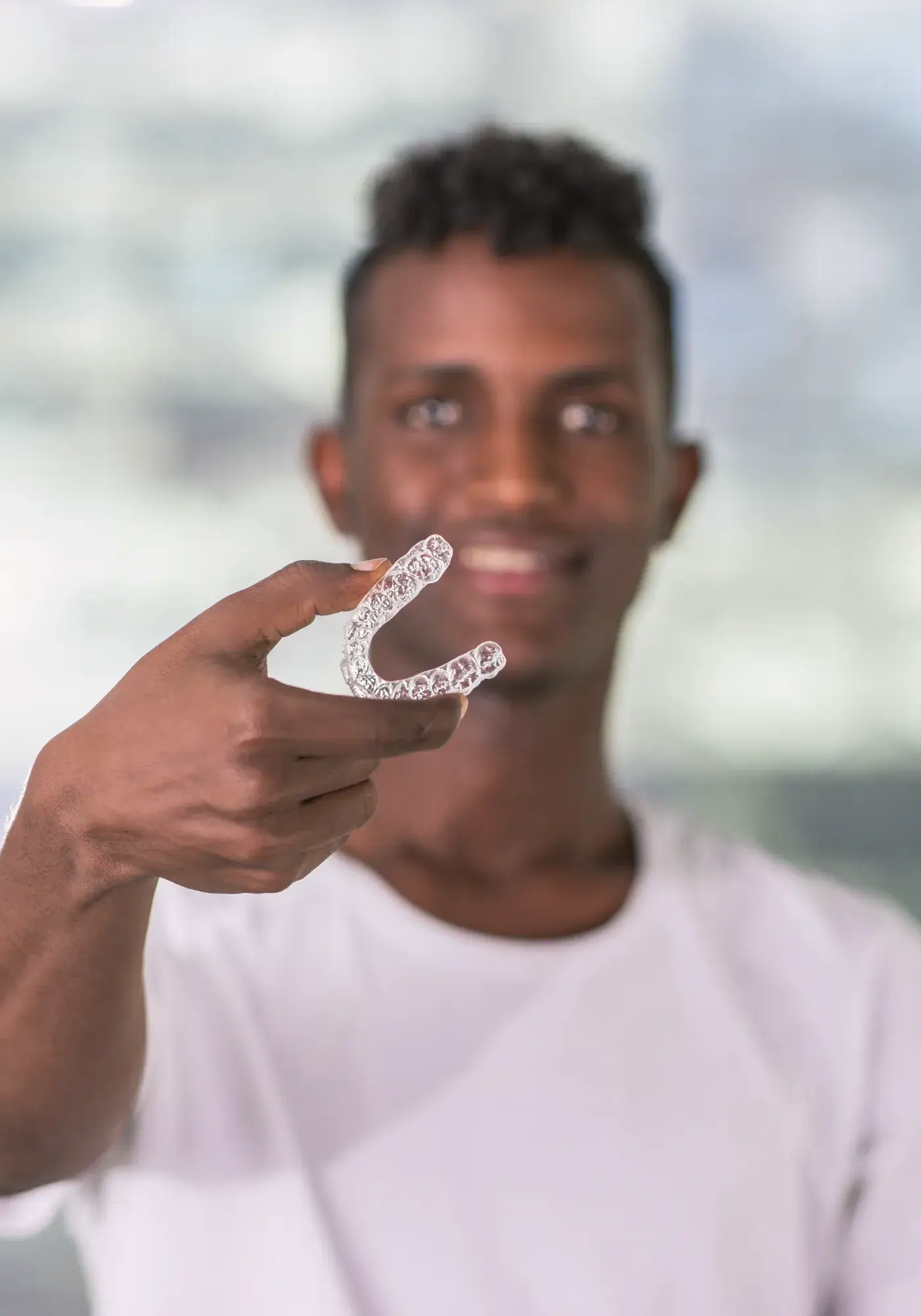 Smiling man holding a clear dental aligner towards the camera.