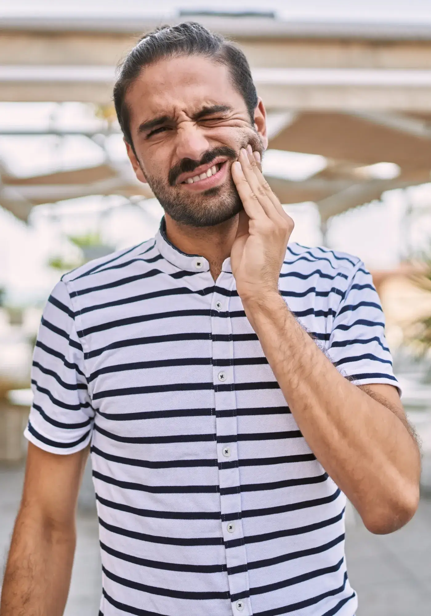 Man in a striped shirt holding his cheek with a pained expression, indicating a toothache.